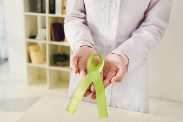 cropped view of doctor holding green ribbon - mental health day