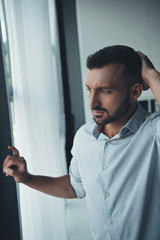 thoughtful lonely man standing at window at home