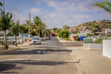 Naklejka premium Street with trees with parked cars with a hill in the background in summer