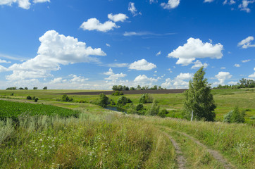Sunny summer landscape with country road,fields,green hills and beautiful clouds in blue sky.River Upa in Tula region,Russia.