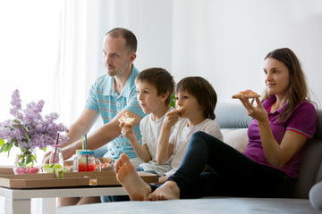 Beautiful young family with children, eating pizza at home and watching TV