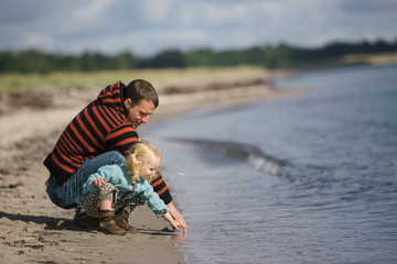 2 year old girl explring the beach with har dad in the early fall