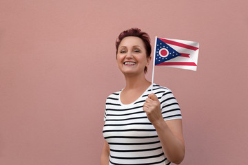 Ohio flag. Woman holding Ohio state flag. Nice portrait of middle aged lady 40 50 years old with a state flag over pink wall on the street outdoors.