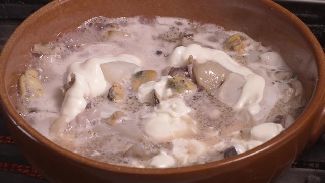 Seafood chowder boiling in a clay pan in UHD