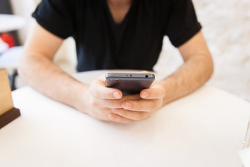 Handsome, young man using his mobile phone in a public area, at the table
