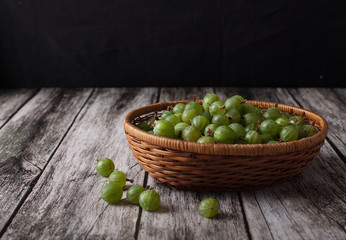 berries of gooseberries in a basket on a wooden background