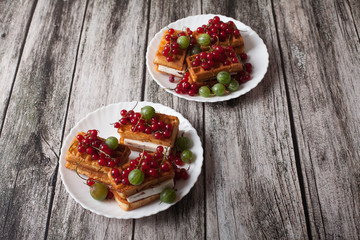 Viennese waffles with berries of red currants and gooseberries lie on a plate on a wooden table