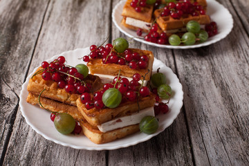 Viennese waffles with berries of red currants and gooseberries lie on a plate on a wooden table