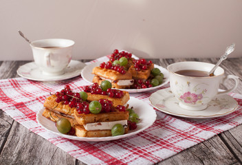 Viennese waffles with berries and a cup of tea stand on a checkered tablecloth on the table