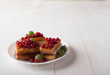 Viennese waffles with red currants and gooseberries lie on a plate on a white wooden table