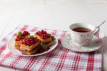 Viennese waffles with berries and a cup of tea stand on a checkered tablecloth on the table