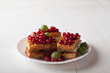 Viennese waffles with red currants and gooseberries lie on a plate on a white wooden table