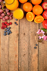 Orange juice, fresh oranges, apples, grapes, raspberries, blueberries and spring flowers on a wooden table - view from above - vertical photo
