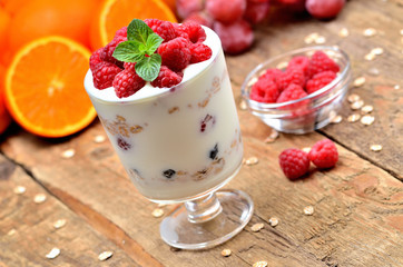 Greek yoghurt, fresh raspberries in a glass and mint leaves, oranges and grapes in background - healthy breakfast concept