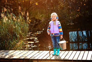 An angler girl with a fishing rod and a bucket with a catch stan