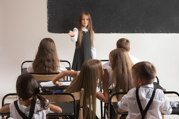 Obraz premium School children in classroom at lesson. The little boys and girls sitting at desks. Back to school, education, classroom, lesson, learn, lifestyle, childhood concept