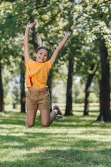 adorable happy child jumping and smiling at camera in park