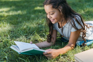 cute smiling child lying on grass and reading book