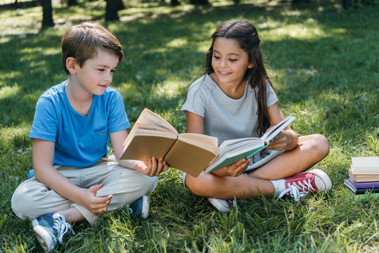 Cute Little Kids Sitting On Grass And Reading Books