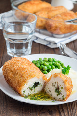 Chicken Kiev, ukrainian cuisine. Cutted chicken cutlet in bread crumbs stuffed with butter and herbs, served with mashed potato and green peas, on brown background, vertical
