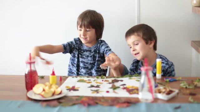 Sweet children, boys, applying leaves using glue while doing arts and crafts in school, autumn time