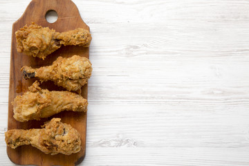 Fried chicken legs on wooden board over white wooden table, top view. Overhead, flat lay, from above. Space for text.