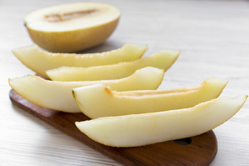 Sliced melon on rustic wooden board over white wooden background, side view. Close-up.