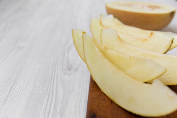 Sliced melon on rustic wooden board over white wooden background, side view. Close-up. Space for text.
