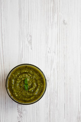 Freshly made basil pesto in a bowl on white wooden surface, view from above. Space for text.