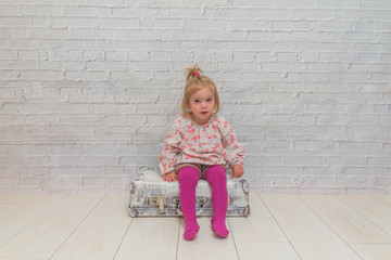 a girl, child with suitcase on white brick wall background