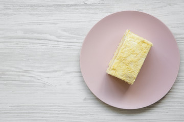 Piece of Napoleon Cake on pink plate over white wooden table, overhead view. Flat lay, from above, top view. Copy space.