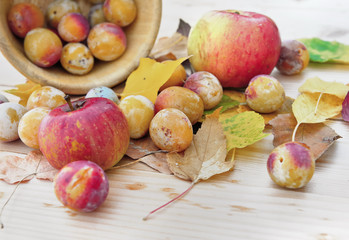 red apples and plums on autumnal leaves put on a wooden table