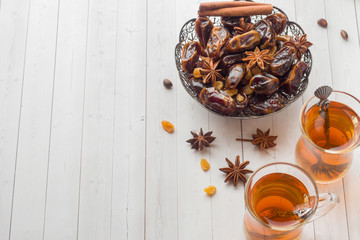 Oriental sweets, dried fruit dates and raisins, cinnamon and star anise in a plate. Turkish tea in glasses on a wooden background.