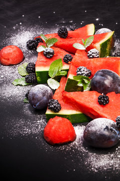 Sliced watermelon with blackberries and mint leaves on black backgroung. Healthy vegetarian food