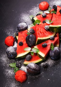 Sliced watermelon with blackberries and mint leaves on black backgroung. Healthy vegetarian food