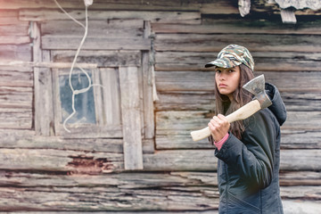 Girl with an ax on his shoulder goes along the wooden old building, looking into the frame.