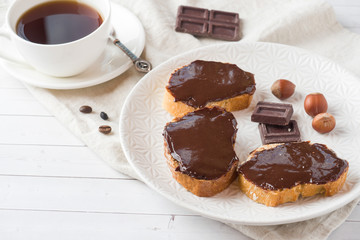 Sandwiches with chocolate hazelnut spread on the plate. Cup of coffee on the table.