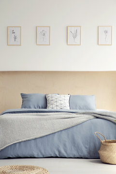 Posters on white wall above blue bed with pillows in simple bedroom interior with basket. Real photo