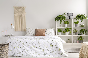 Close to nature bright bedroom interior with many green plants beside a big bed. Woven tapestry...