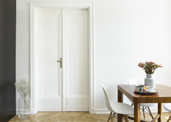 A white wall with double door next to a wooden breakfast table and chairs in a dining room...