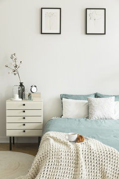 Croissant and coffee for breakfast on a blanket on a bed in a pastel color bedroom interior. Nightstand by the bed. Real photo.