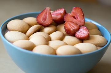 Strawberry pudding in blue bowl with fresh red cut strawberries and rounded ladyfingers on the top