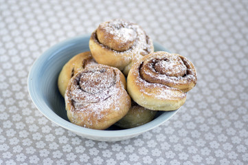 Cinnamon snails called kanelbullar, very tasty sweet rolls in blue bowl on floral pattern tablecloth
