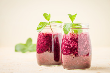 Blueberry smoothie decorated with fresh green mint leaves and raw ripe berries on yellow pastel background.