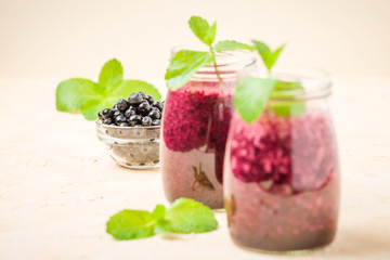 Blueberry smoothie decorated with fresh green mint leaves and raw ripe berries on yellow pastel background.