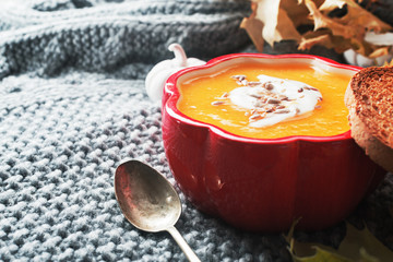 Fall pumpkin cream soup with seeds in red ceramic bowl.