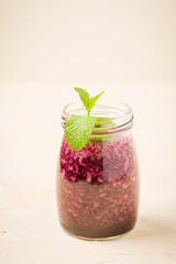 Blueberry smoothie decorated with fresh green mint leaves and raw ripe berries on yellow pastel background.