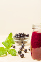 Currant smoothie decorated with fresh green mint leaves and raw ripe berries on yellow pastel background.