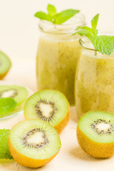 Fototapeta na wymiar Kiwi smoothie decorated with fresh green mint leaves and raw ripe cut fruit on yellow pastel background.