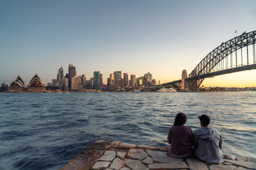 Naklejka premium Romantyczna para patrzy na panoramę Sydney o zmierzchu w Sydney, Nowa Południowa Walia, Australia.